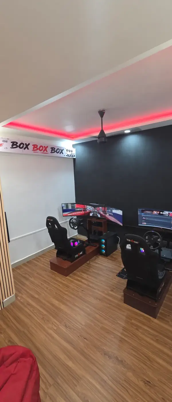 The floor at BOXBOXBOX Guindy — both racing simulator rigs side by side under a BOX BOX BOX banner and a red LED ceiling cove, with a beanbag on the wooden floor for whoever is waiting.
